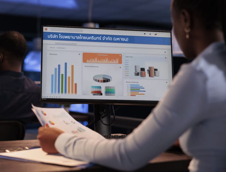 Office employee analyzing business charts on computer and documents, looking at online research data to create presentation. Working with information on report, statistics on pc.